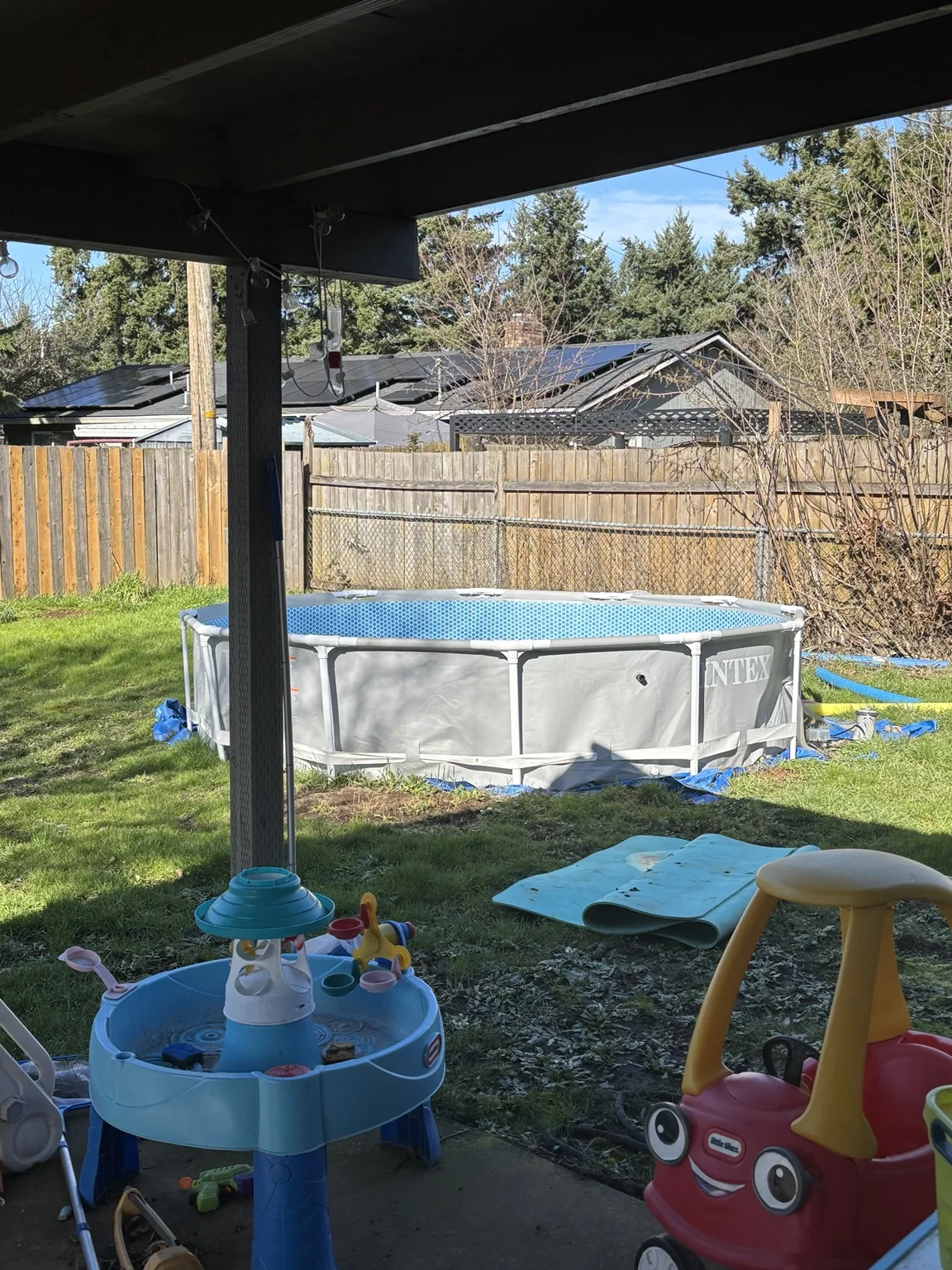 Above-ground frame pool with a gray liner and metal supports in a fenced backyard before removal