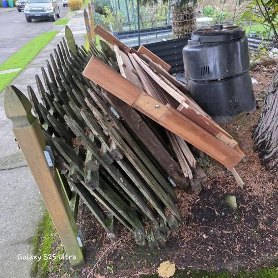 Detached wooden fence panels and loose boards stacked beside a sidewalk before pickup