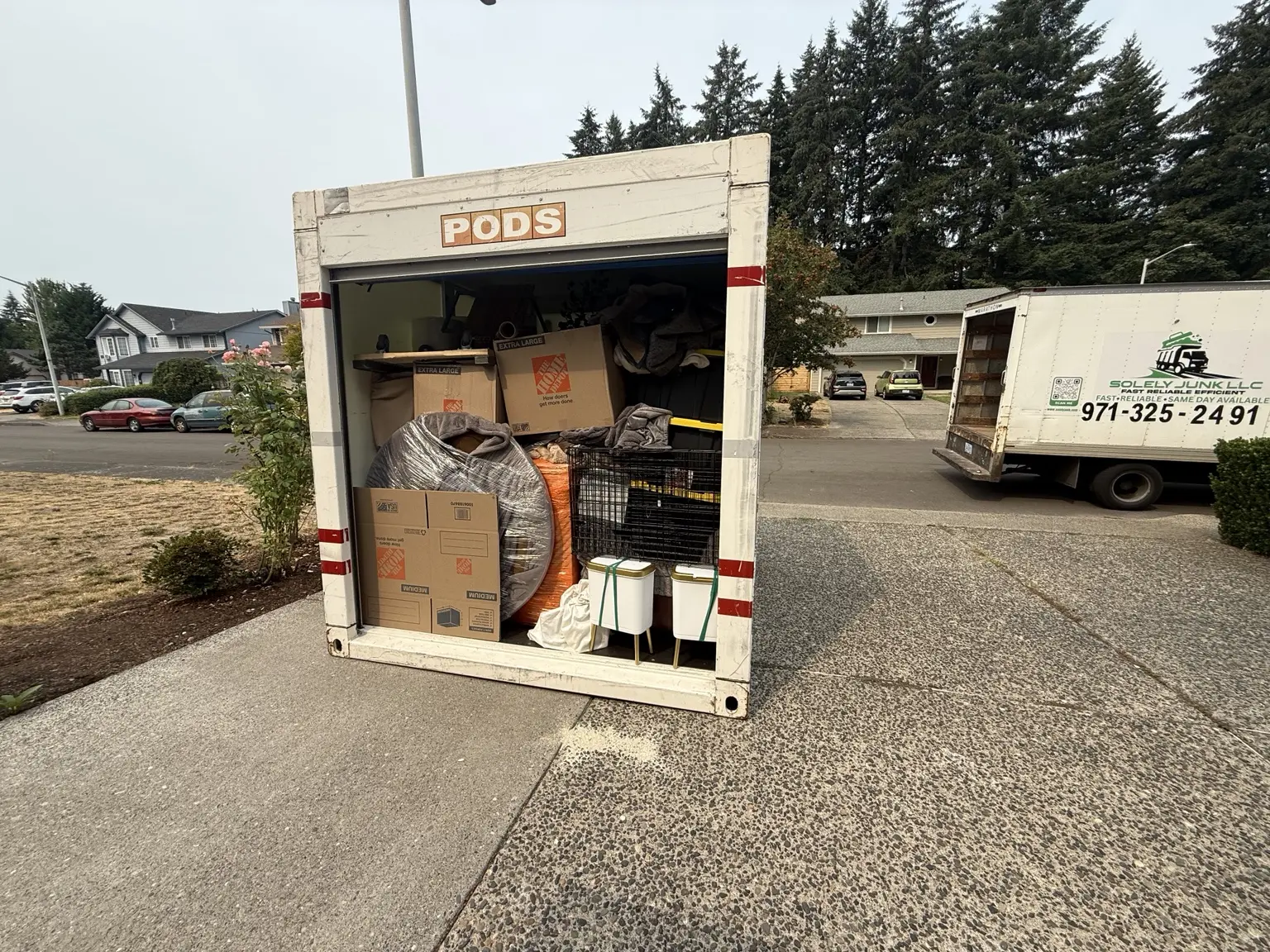 Boxes and household belongings inside an open portable storage container beside the crew truck.